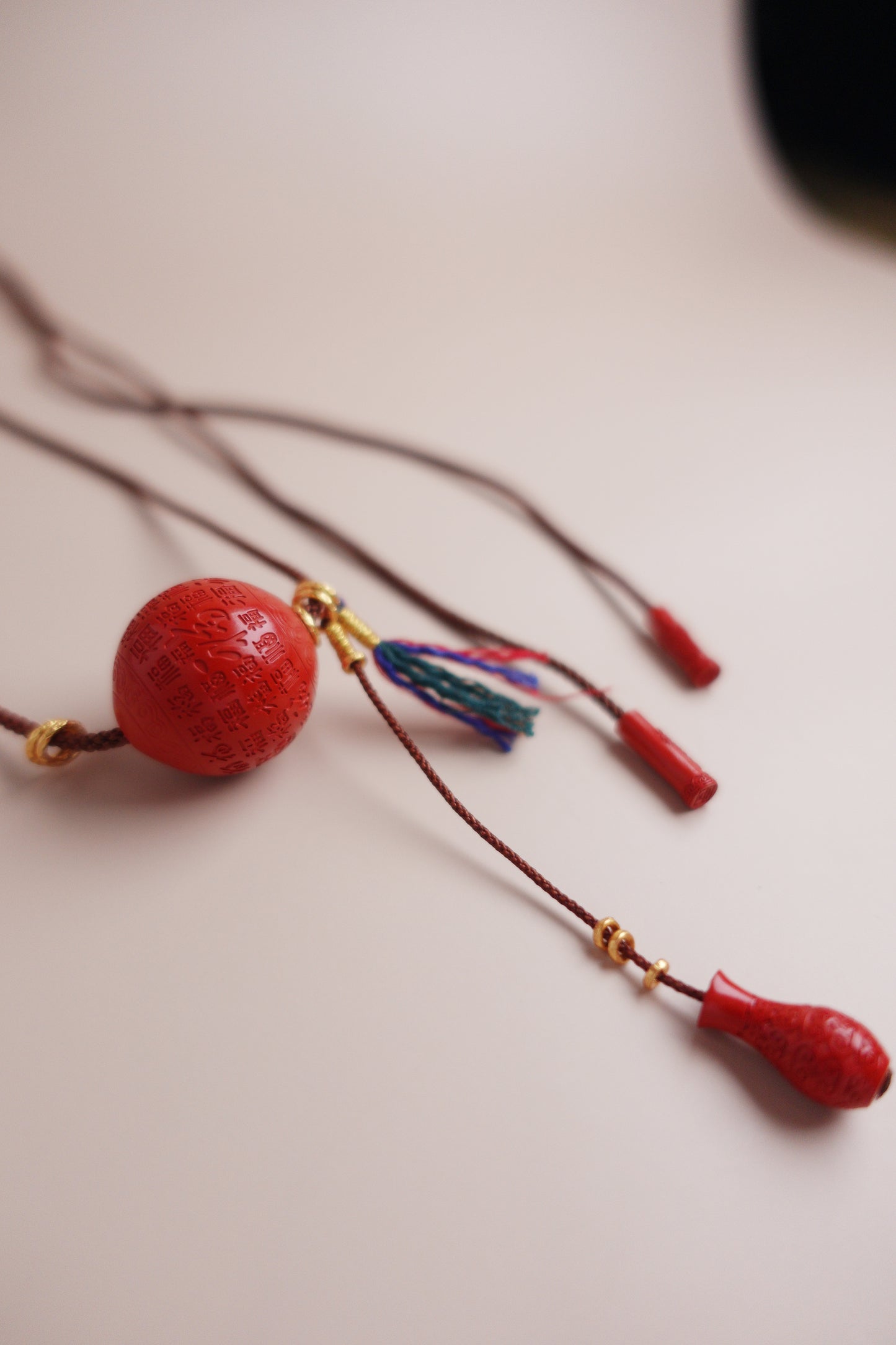 Pendant necklace featuring carved red cinnabar cloud-vase charm on adjustable coffee cord with Tibetan tassel and gold-vermeil fittings.