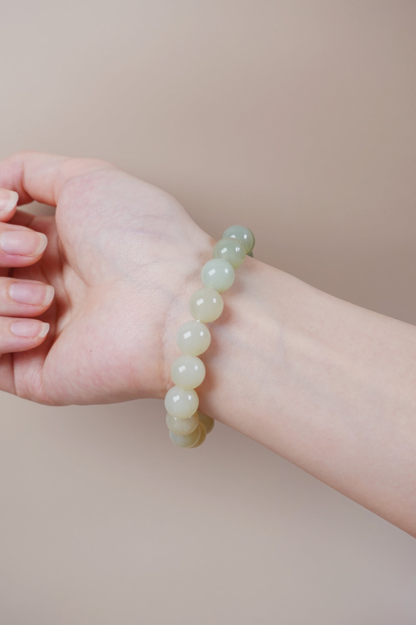 10mm pale green Hetian jade gradient bracelet, symbolic Wood element jewelry.Hetian jade bracelet in soft green gradient worn on wrist, Heart Chakra balance and grounding