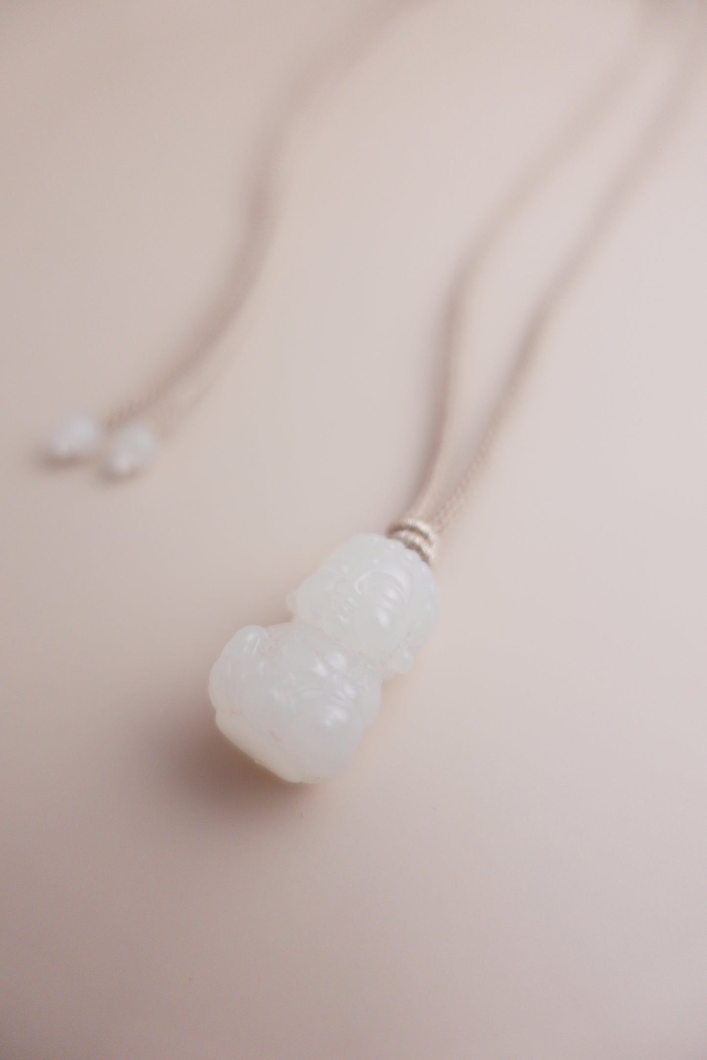 Serene Beginnings necklace featuring a Hetian white jade Baby Buddha carving suspended on a braided silk-cotton cord