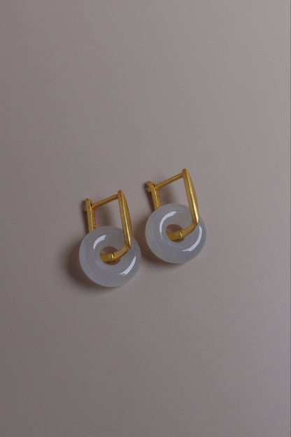 Pair of earrings with white stones and gold accents on a beige background