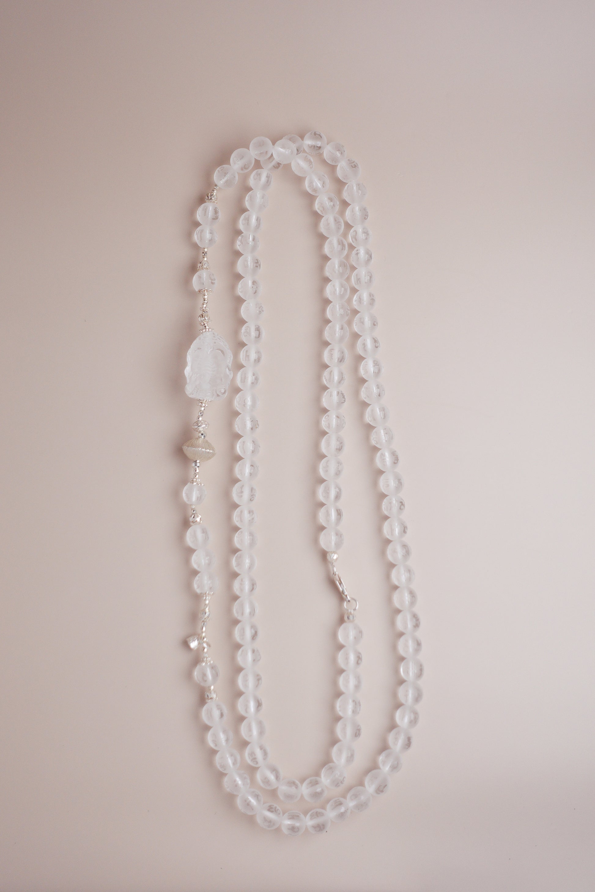Frosted clear quartz mala necklace with Om Mani Padme Hum engraving and carved Baby Ganesha charm on silver accents.